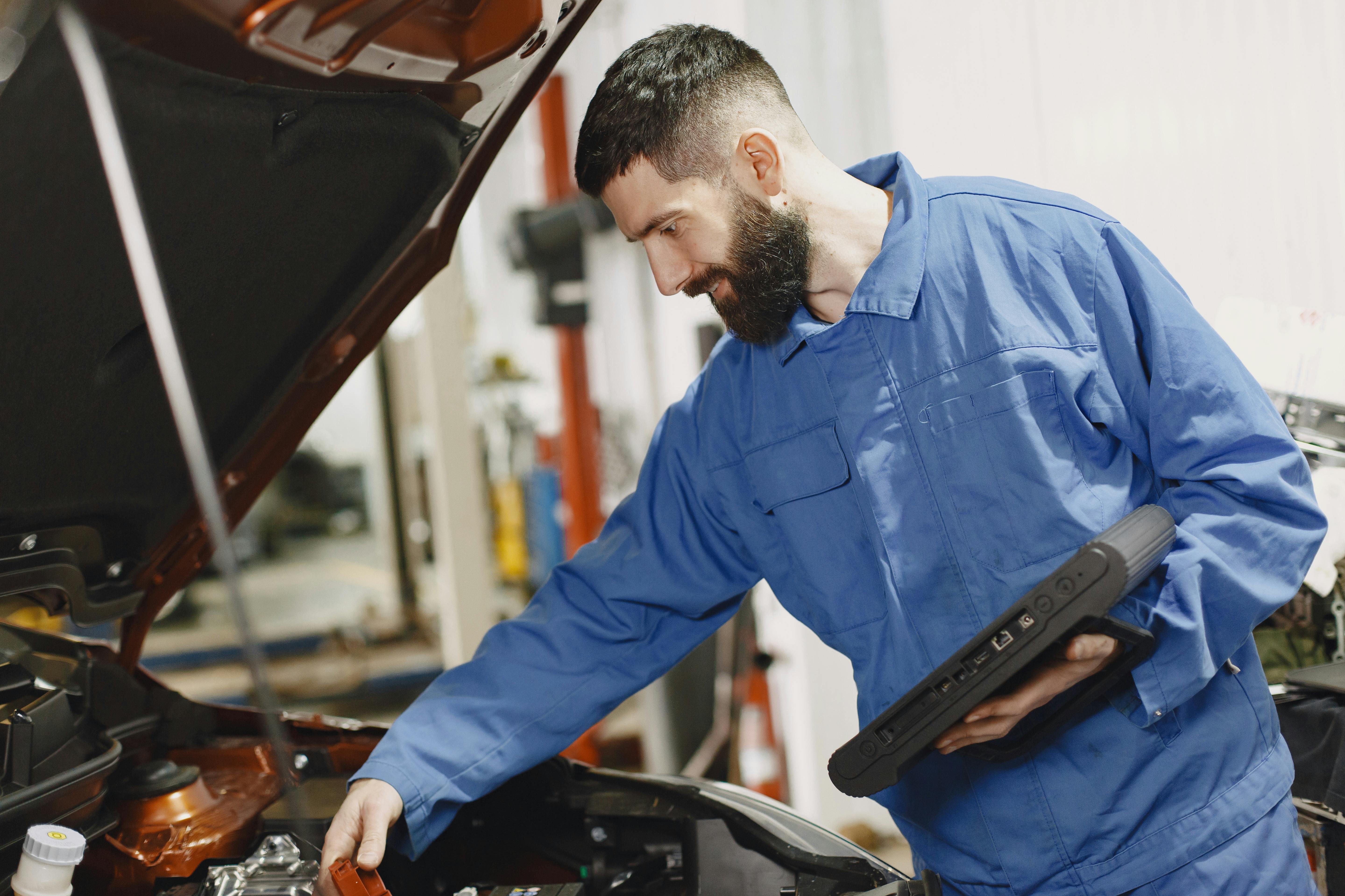 Auto electrician using a diagnostic tablet beside an open bonnet.